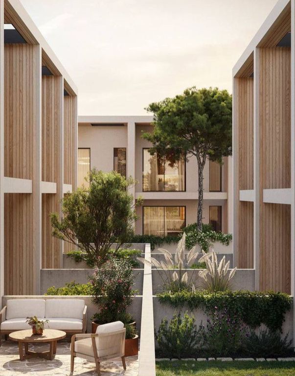 Modern courtyard between two beige concrete buildings with lush green plants and outdoor seating.
