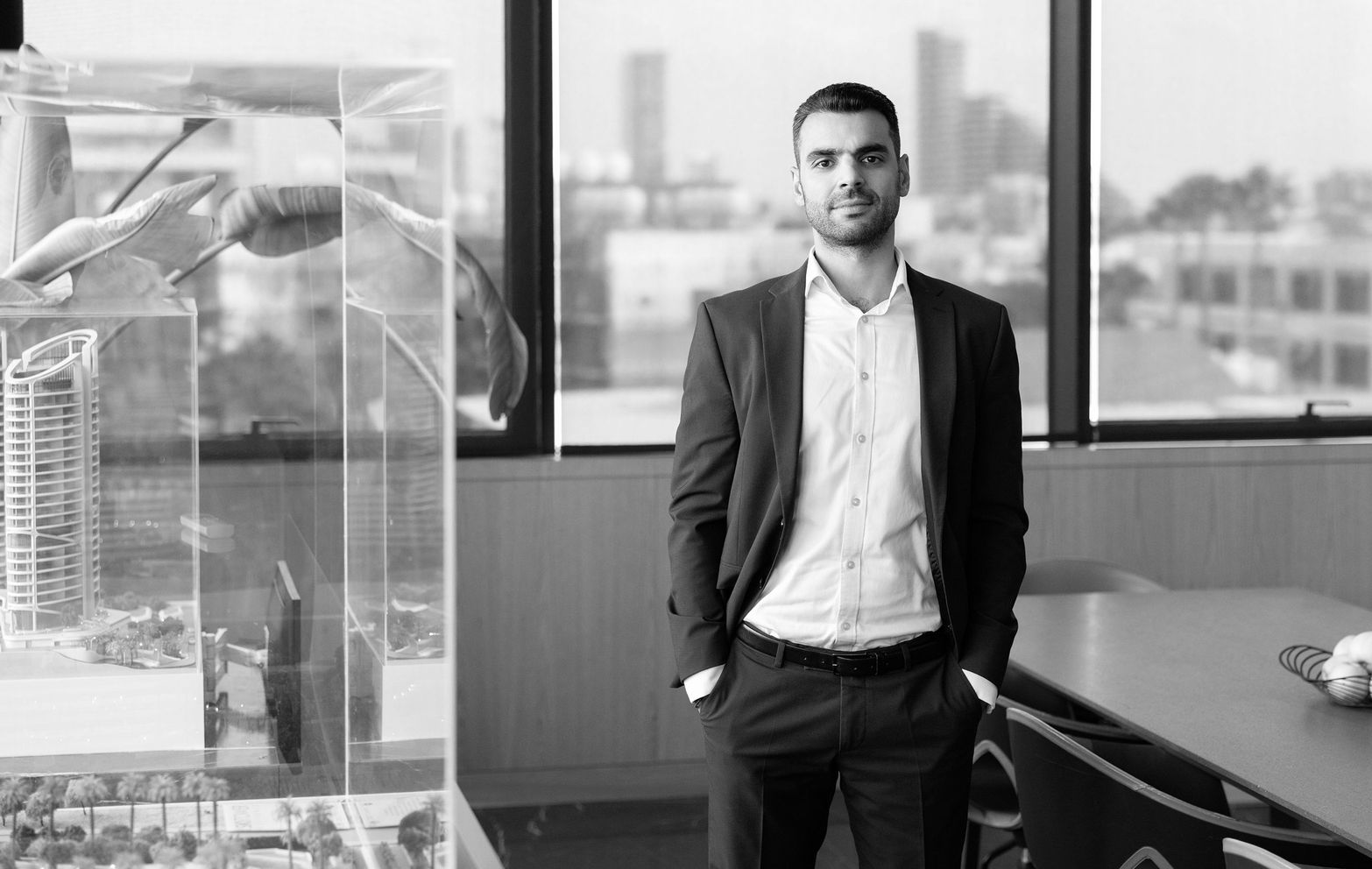 Man in a suit stands in a modern office, a building model beside him.