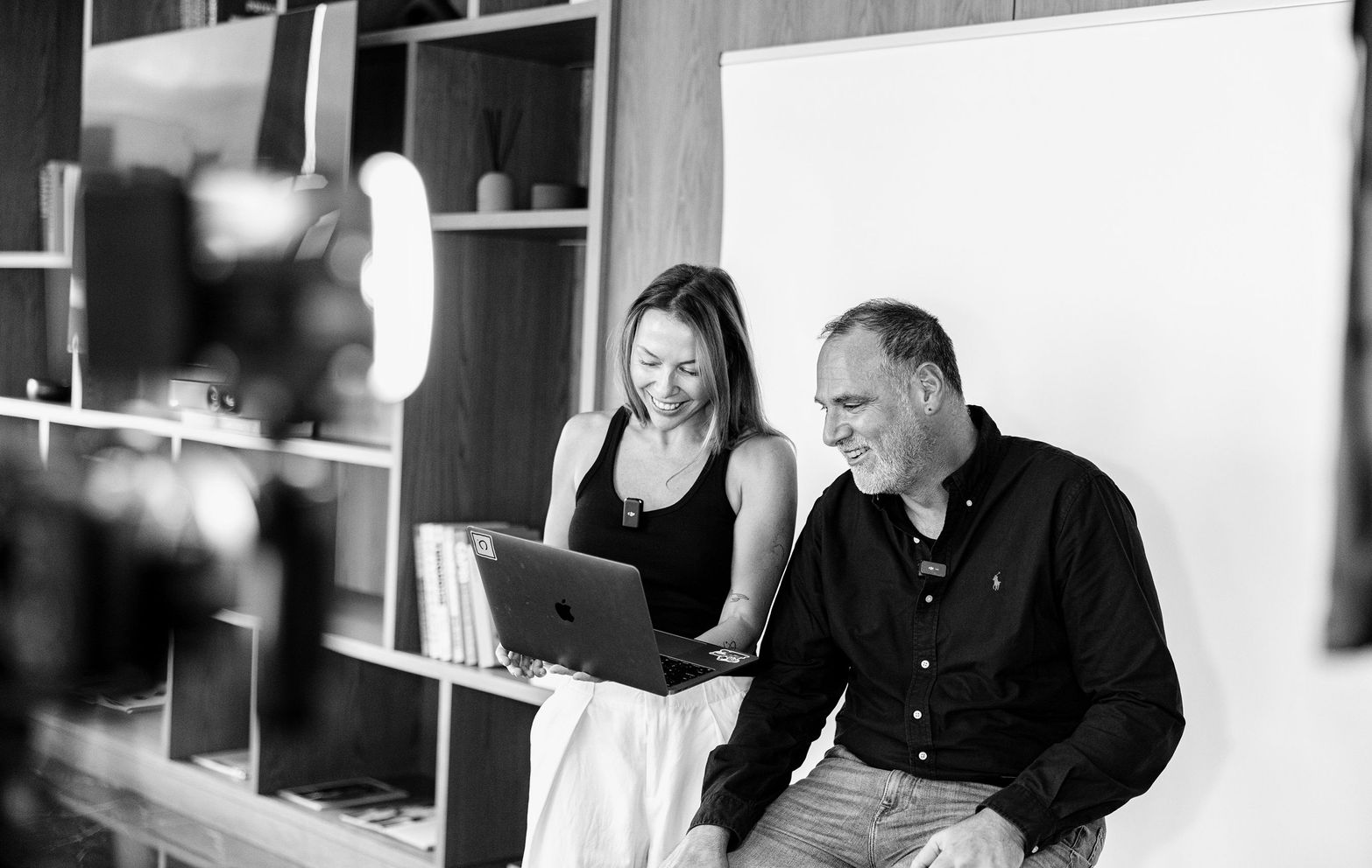 Two smiling professionals collaborating on a laptop during a black and white studio session.
