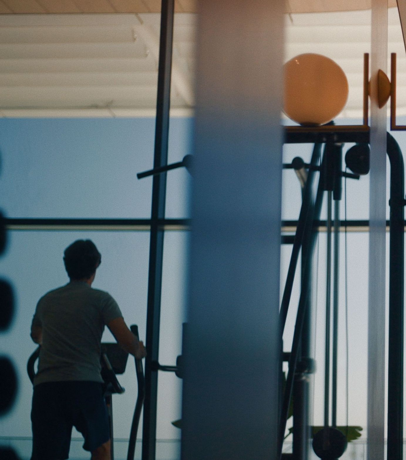 Person exercising on a fitness machine in a bright gym with large windows.