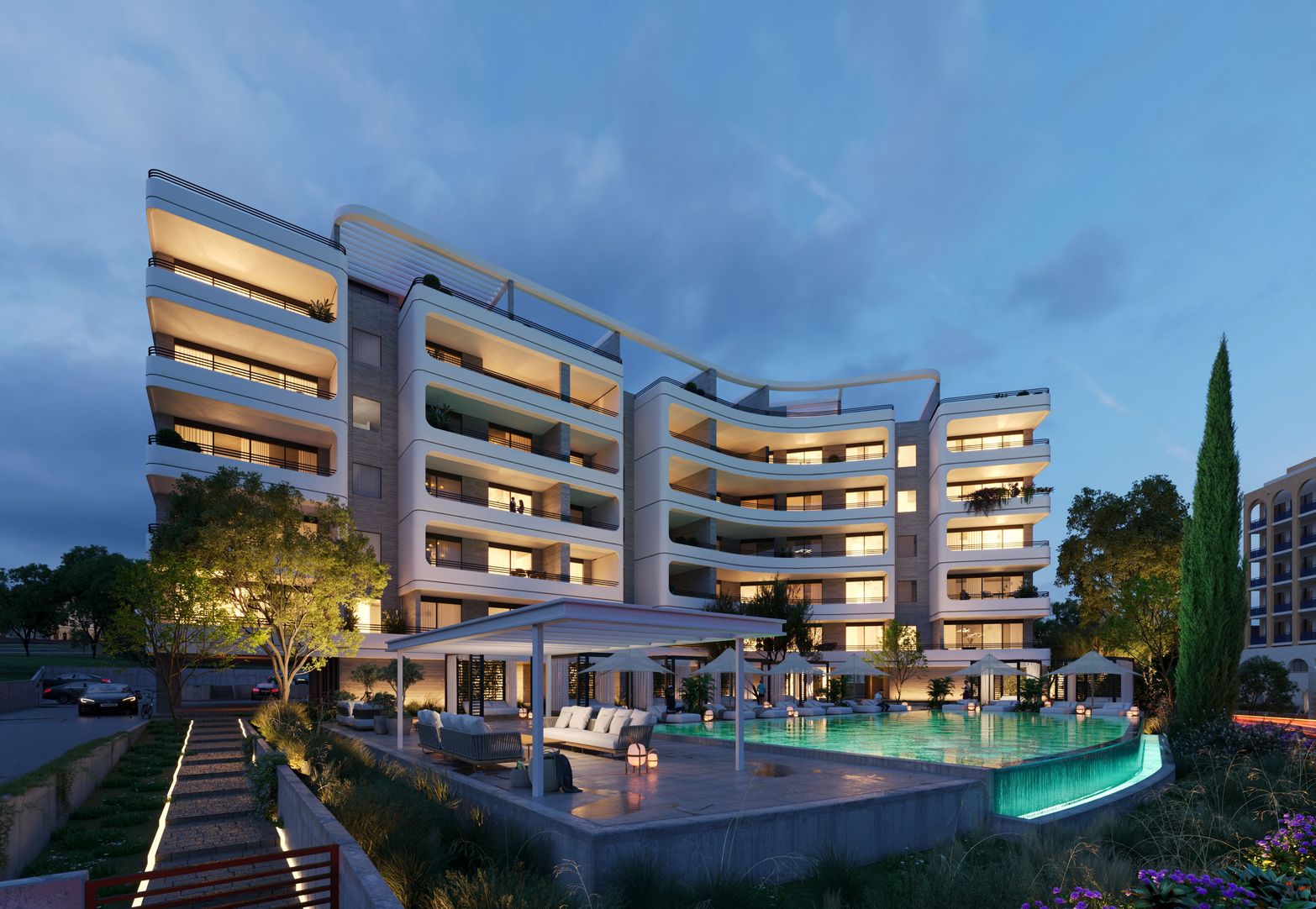 Luxury apartment building with curved architecture, illuminated pool, and outdoor lounge at night.