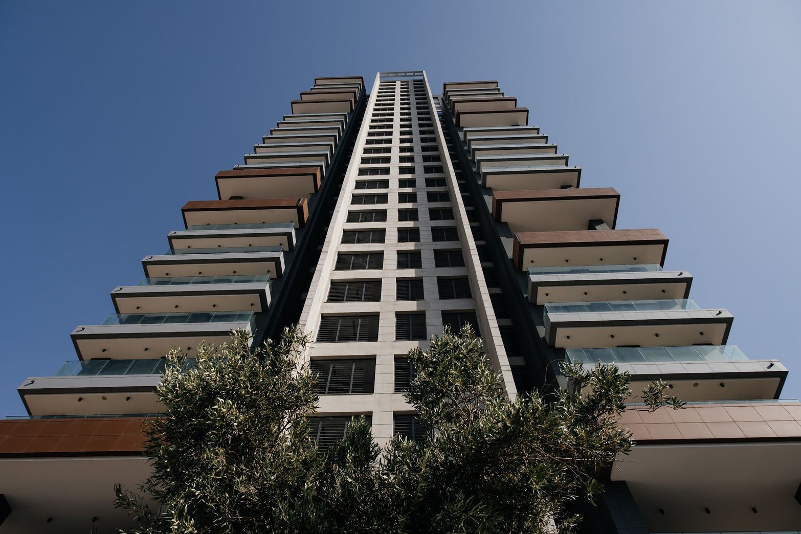 Modern tiered skyscraper from a low angle against a clear blue sky.