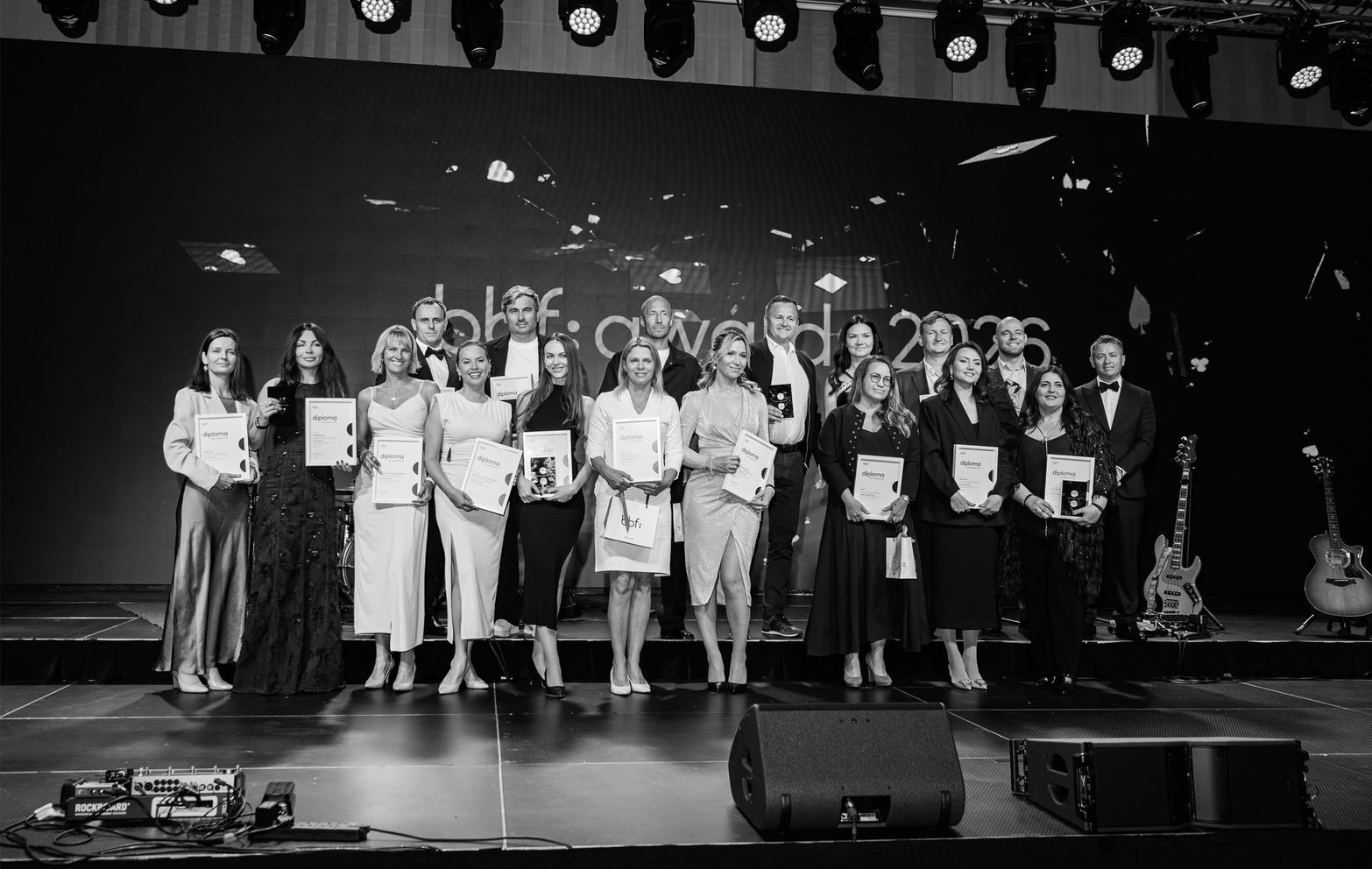 Group of formally dressed people holding awards on stage at an awards ceremony.