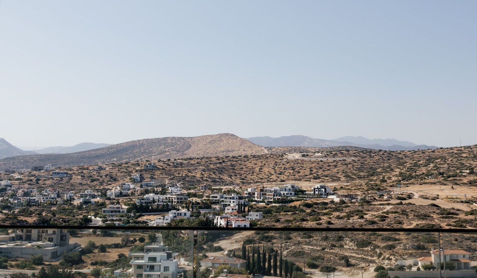 A village surrounded by dry, rolling hills under a bright, clear sky, viewed from above.