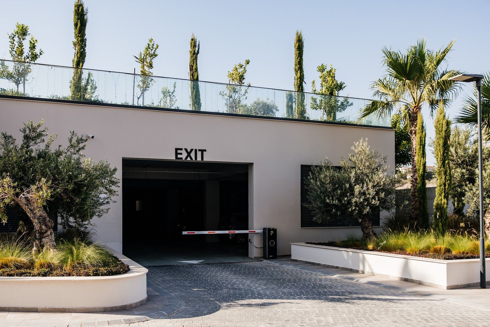 Modern parking garage exit with an automated barrier and lush green landscaping.