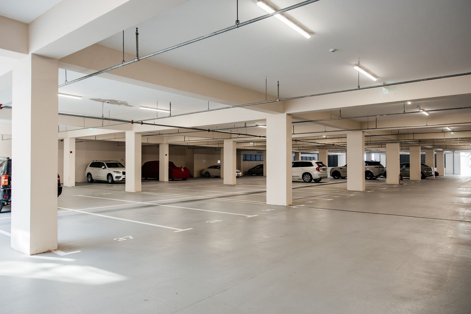 Clean, brightly lit underground parking garage with concrete pillars and several parked cars.