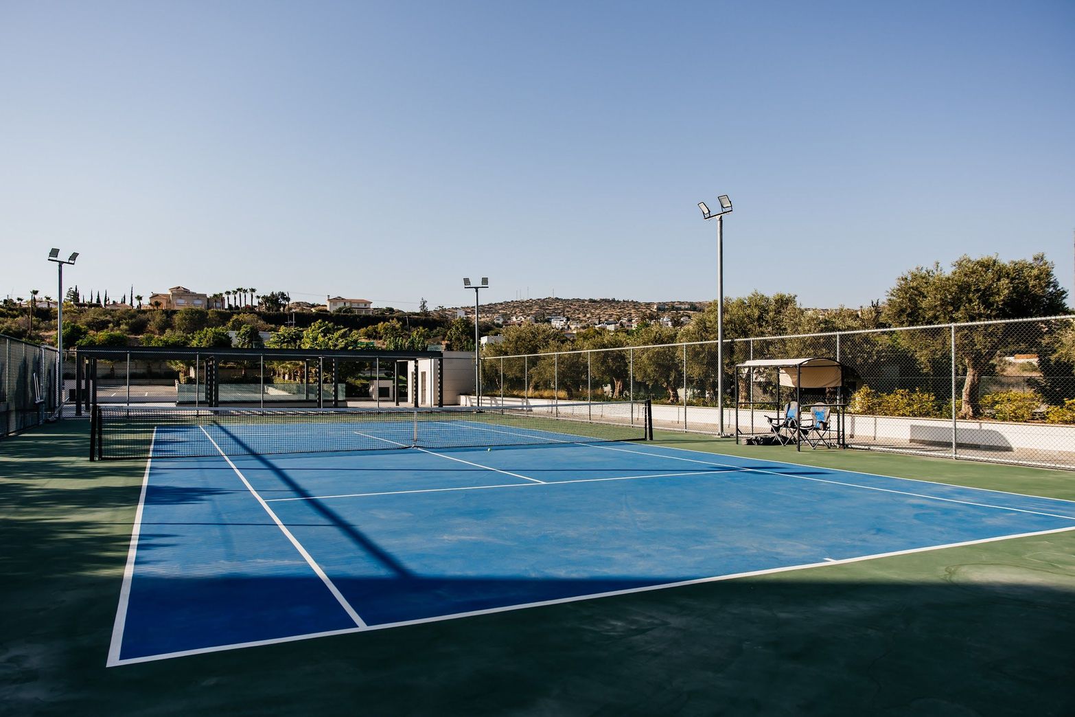 An empty outdoor blue tennis court with white lines on a clear day.