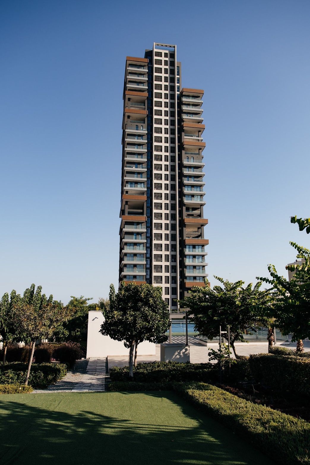 Tall modern high-rise building with many windows and balconies against a clear blue sky.