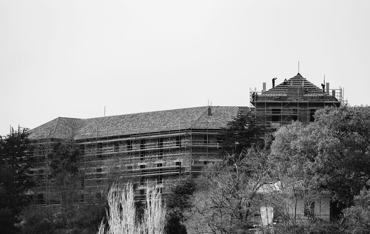 Large historic building in black and white, featuring scaffolding and surrounding trees.