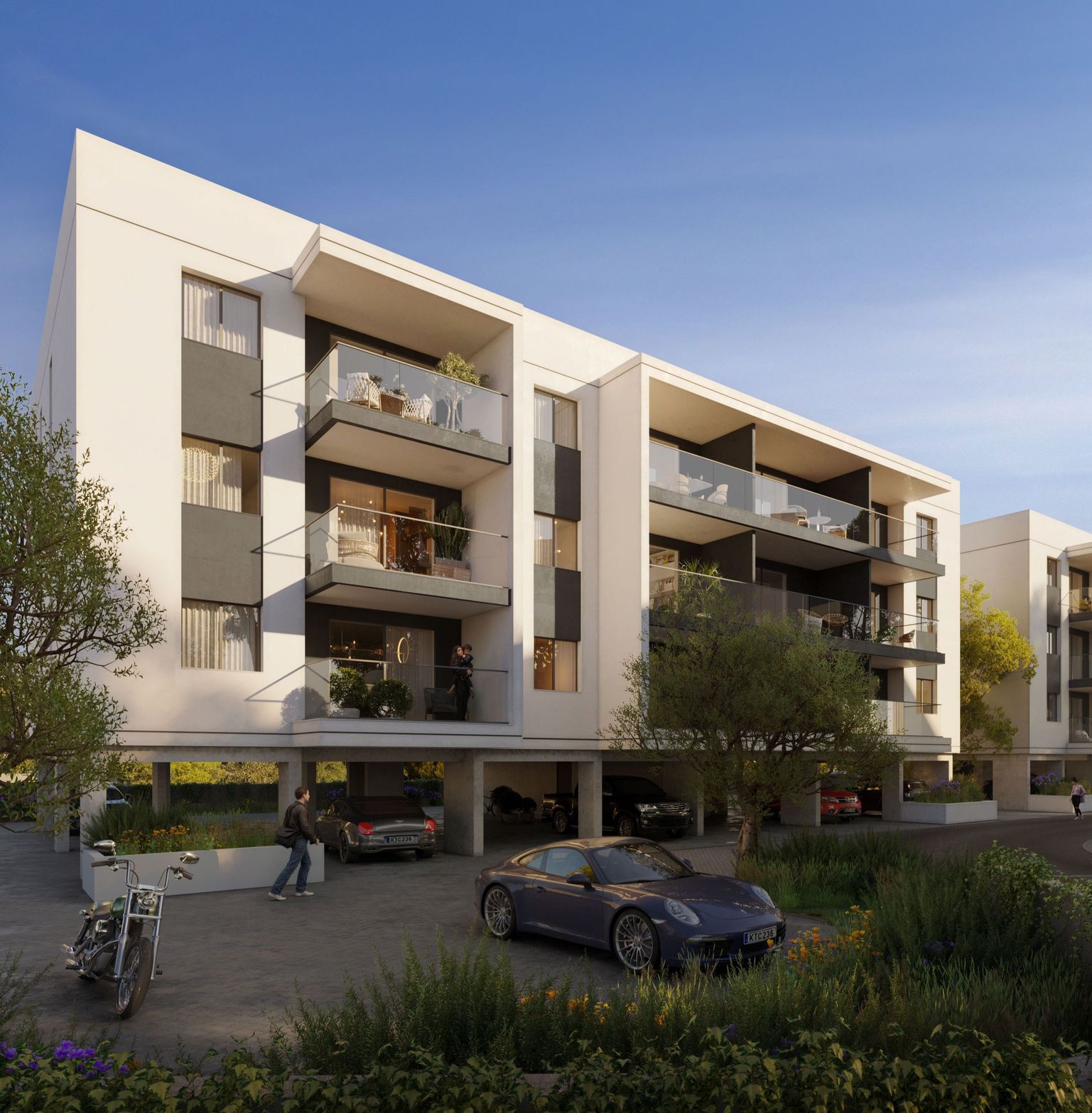 Modern white and gray apartment building with balconies, covered parking, and landscaping.