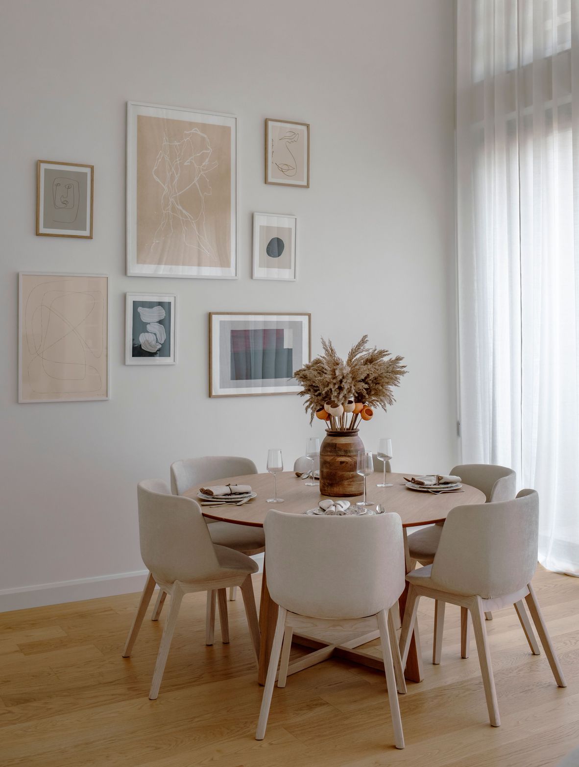 Modern dining room with round table, six chairs, and a gallery wall with framed art.