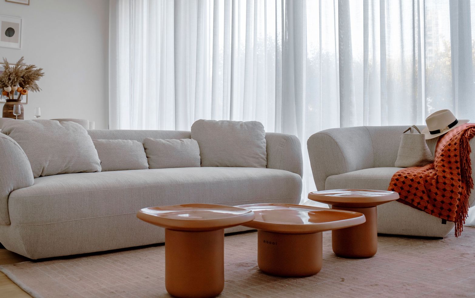A modern living room featuring a light gray sofa, armchair, and unique orange coffee tables.