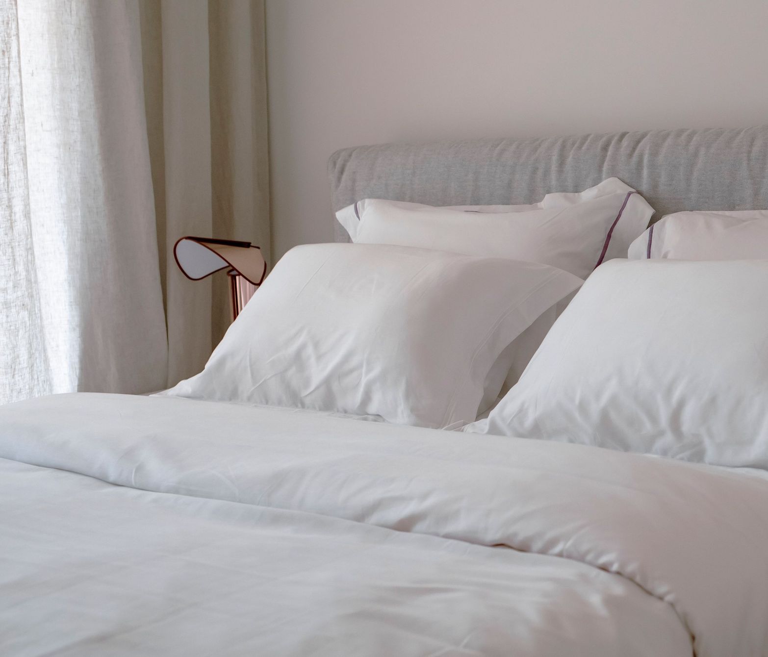 A bed with fresh white duvet and multiple white pillows against a light headboard.