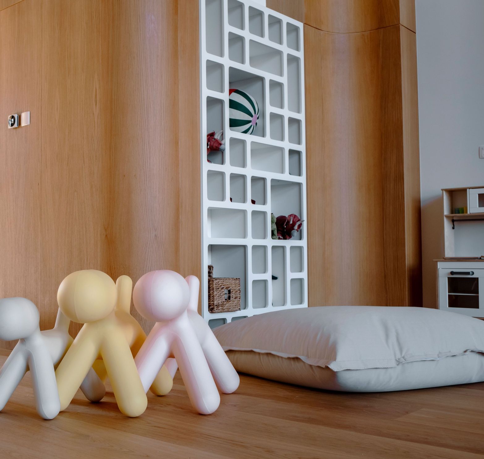 Colorful abstract figures sit on a wooden floor in a modern room with geometric shelf.