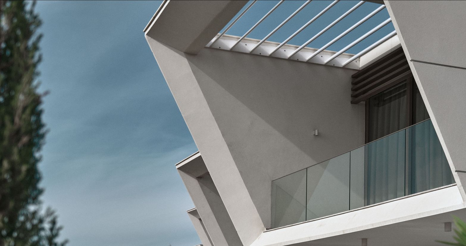 Modern building featuring sharp geometric angles, a glass balcony, and a clear sky.