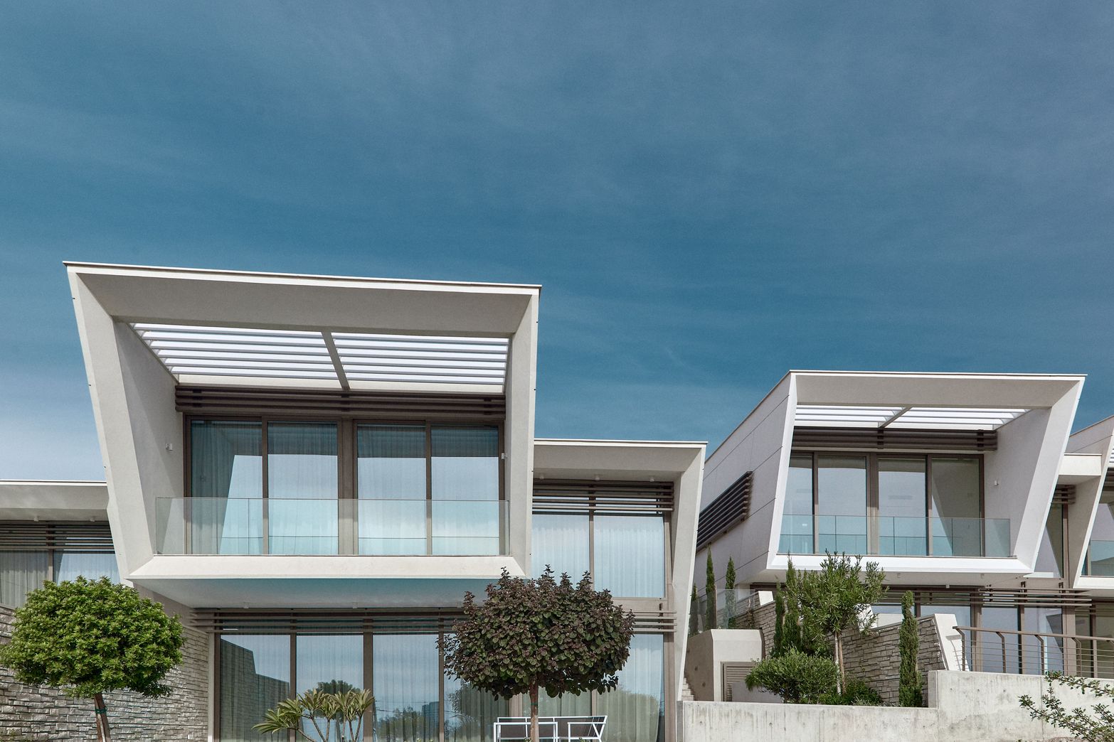 Modern geometric white buildings with large windows and balconies under a clear blue sky.