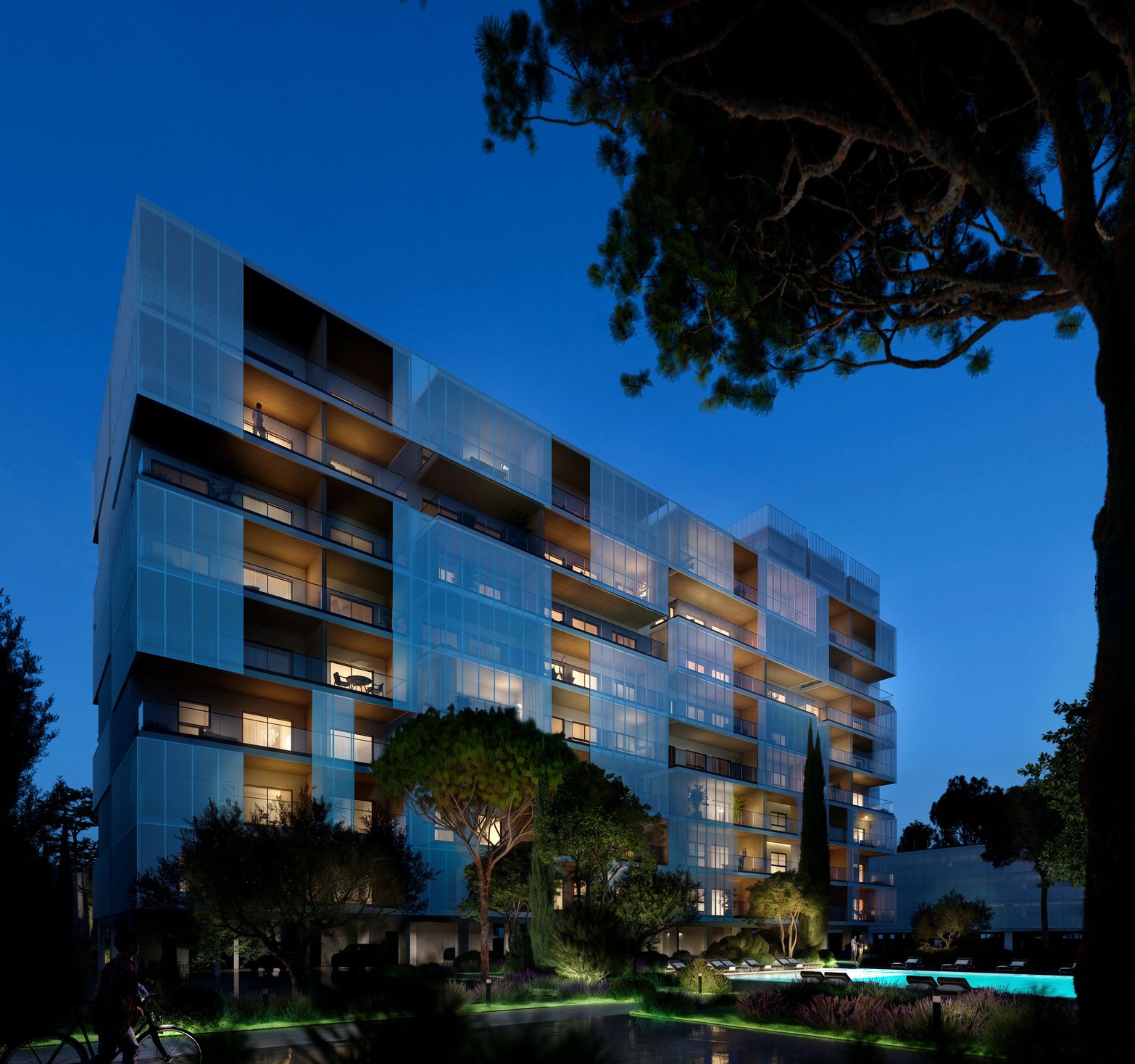 Modern building with illuminated glass facade, swimming pool, and landscaped gardens at night.