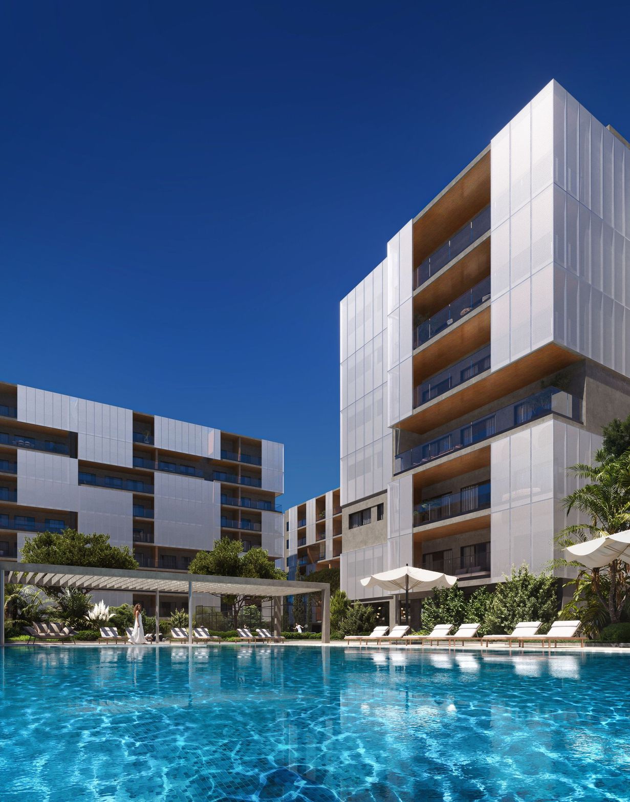 Modern hotel buildings overlook a sparkling blue swimming pool with lounge chairs.
