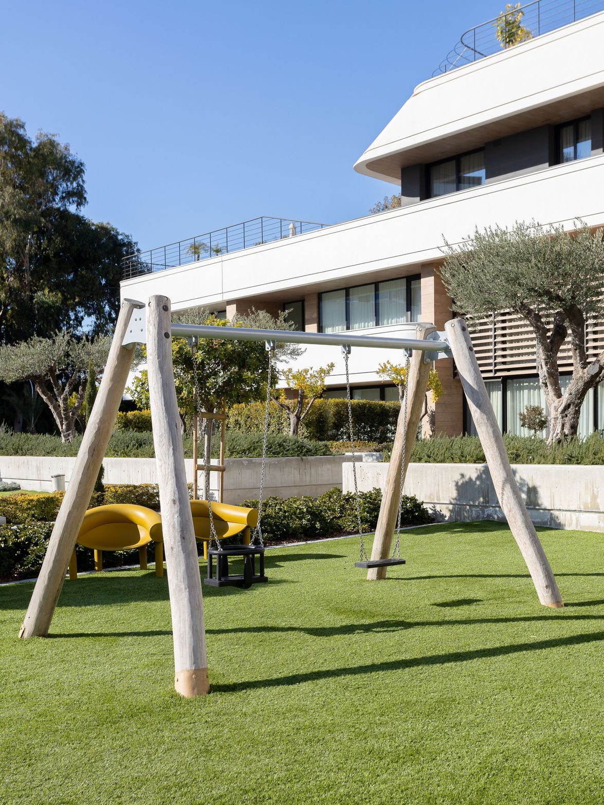 Wooden swing set on a lush green lawn in front of a modern building.