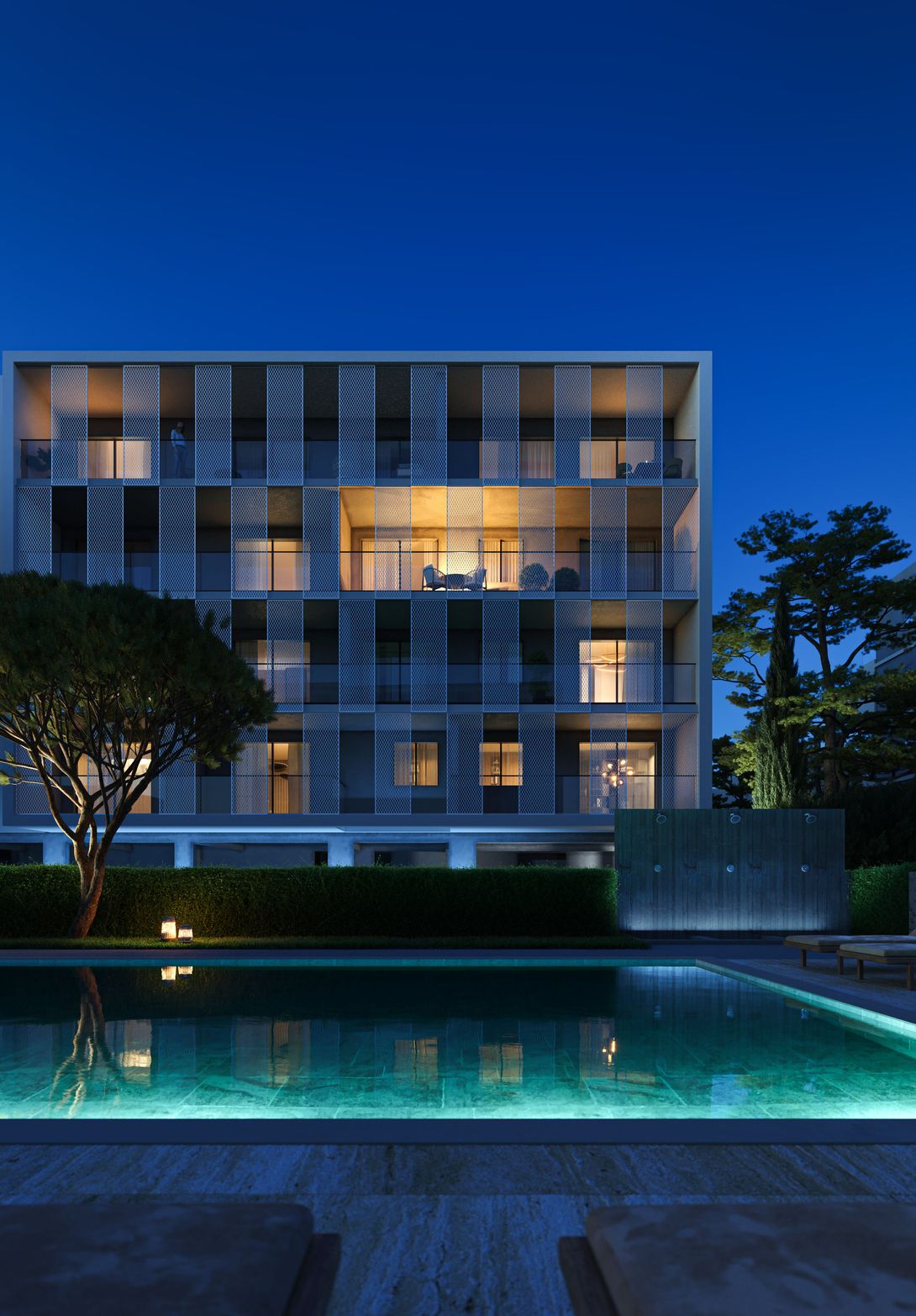 Modern building with illuminated balconies beside a glowing blue swimming pool at night.