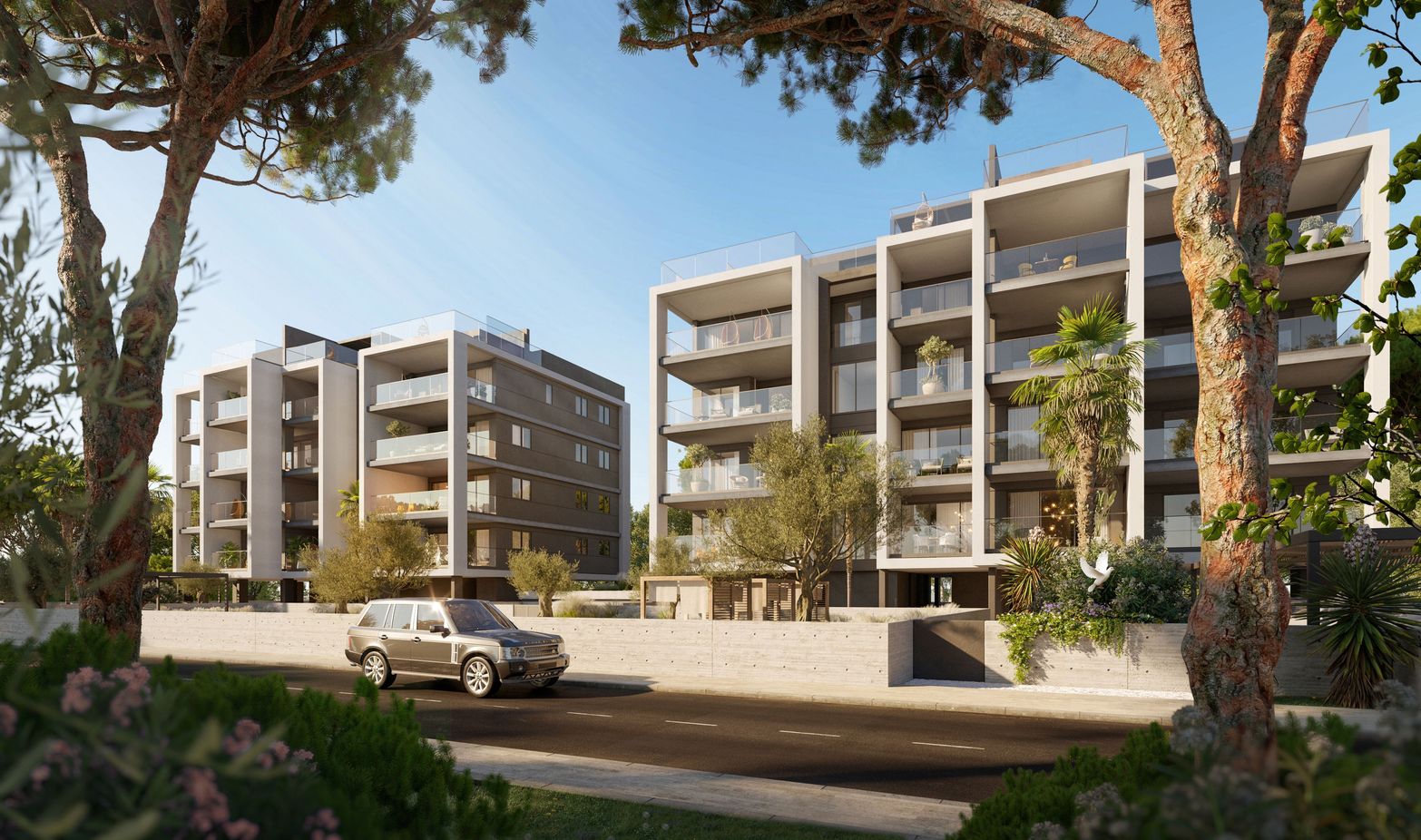 Modern apartment buildings with balconies, a car on a road, and lush trees.