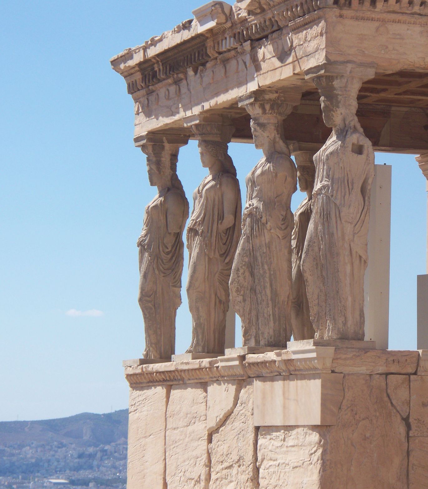 Ancient Greek Caryatid statues supporting a temple roof against a clear blue sky.