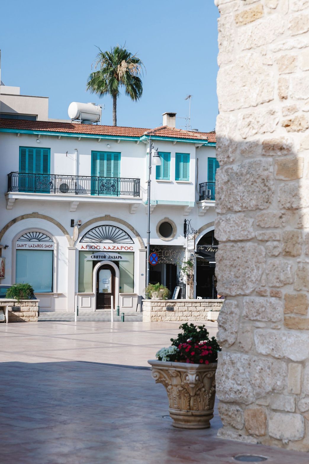 White building with teal shutters, balconies, and a tall palm tree under a clear sky.