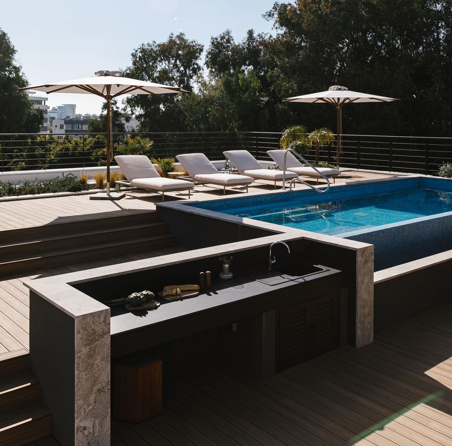 Luxury outdoor swimming pool area with wooden deck, lounge chairs, umbrellas, and a modern bar.
