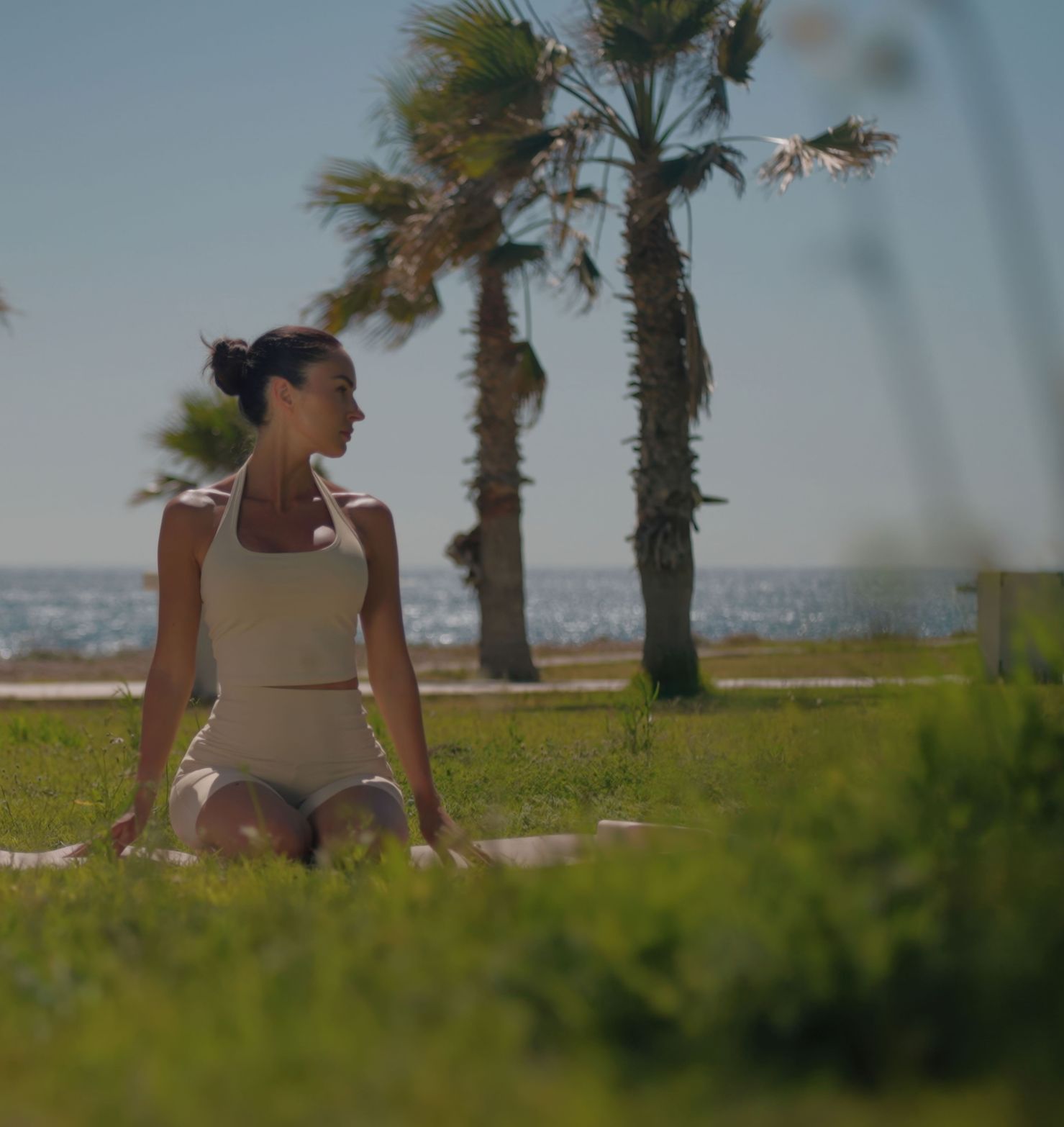 Young woman in activewear meditating outdoors by the sea under palm trees.