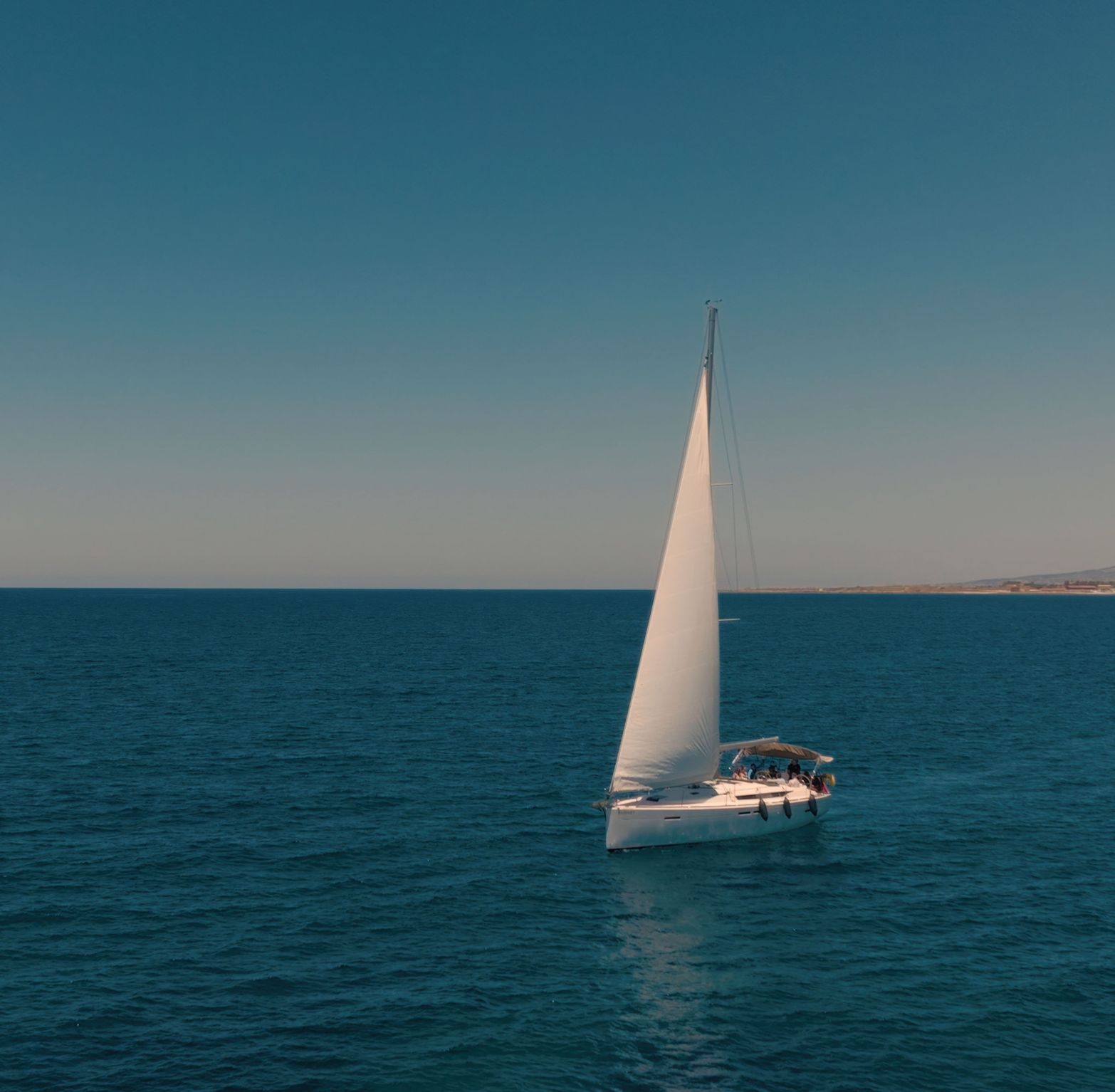 White sailboat with sails unfurled gliding on a vast blue ocean under clear sky.