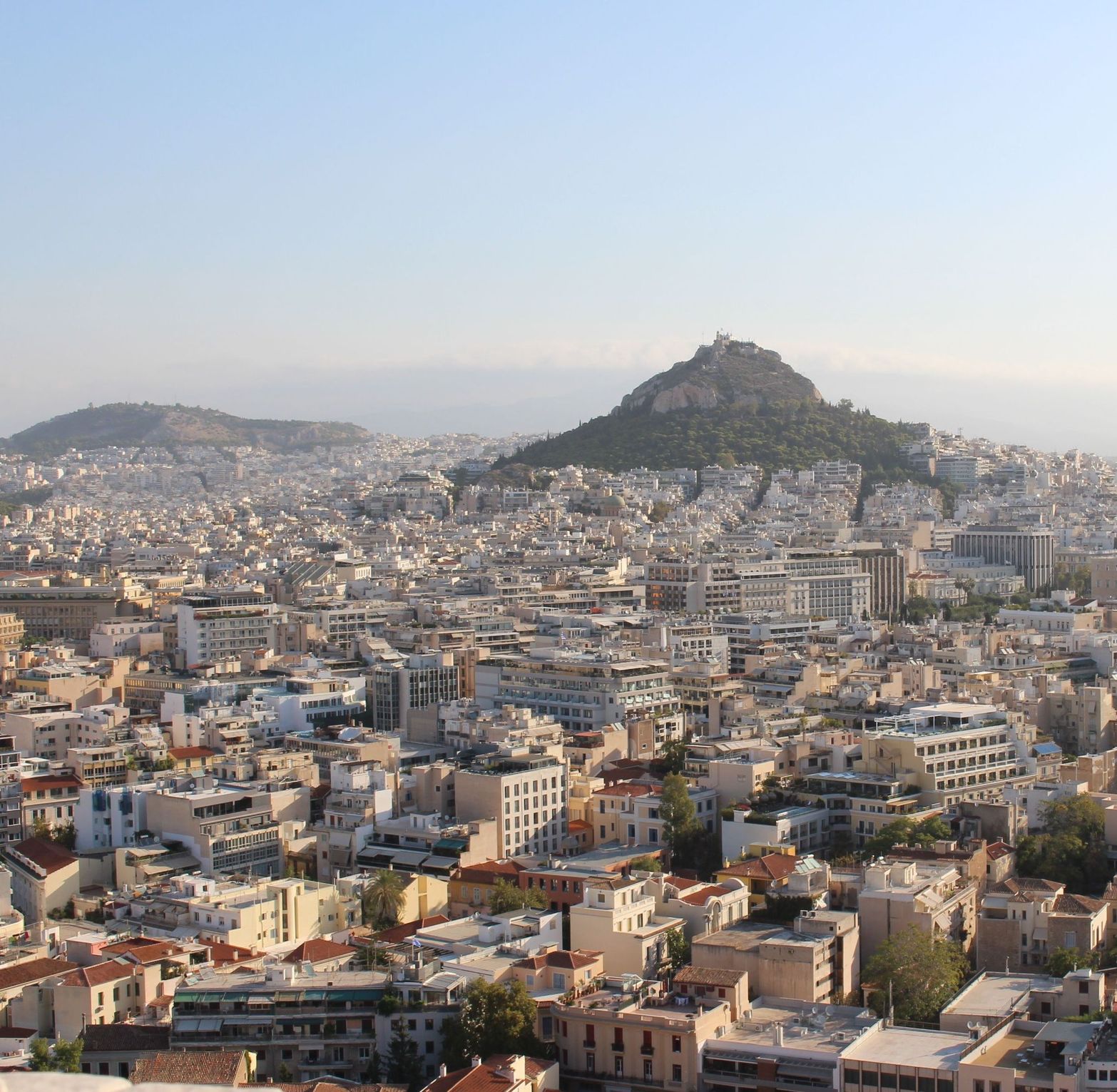 Aerial view of a sprawling city with many buildings and a large mountain under a clear sky.