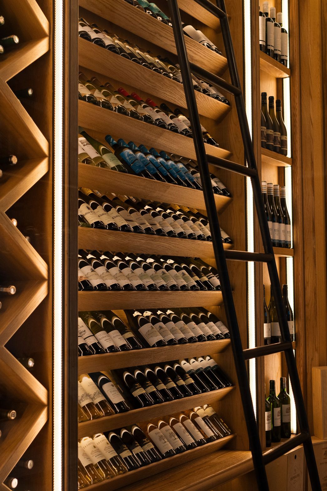 A luxurious wine cellar features many bottles on lit wooden shelves with a tall ladder.
