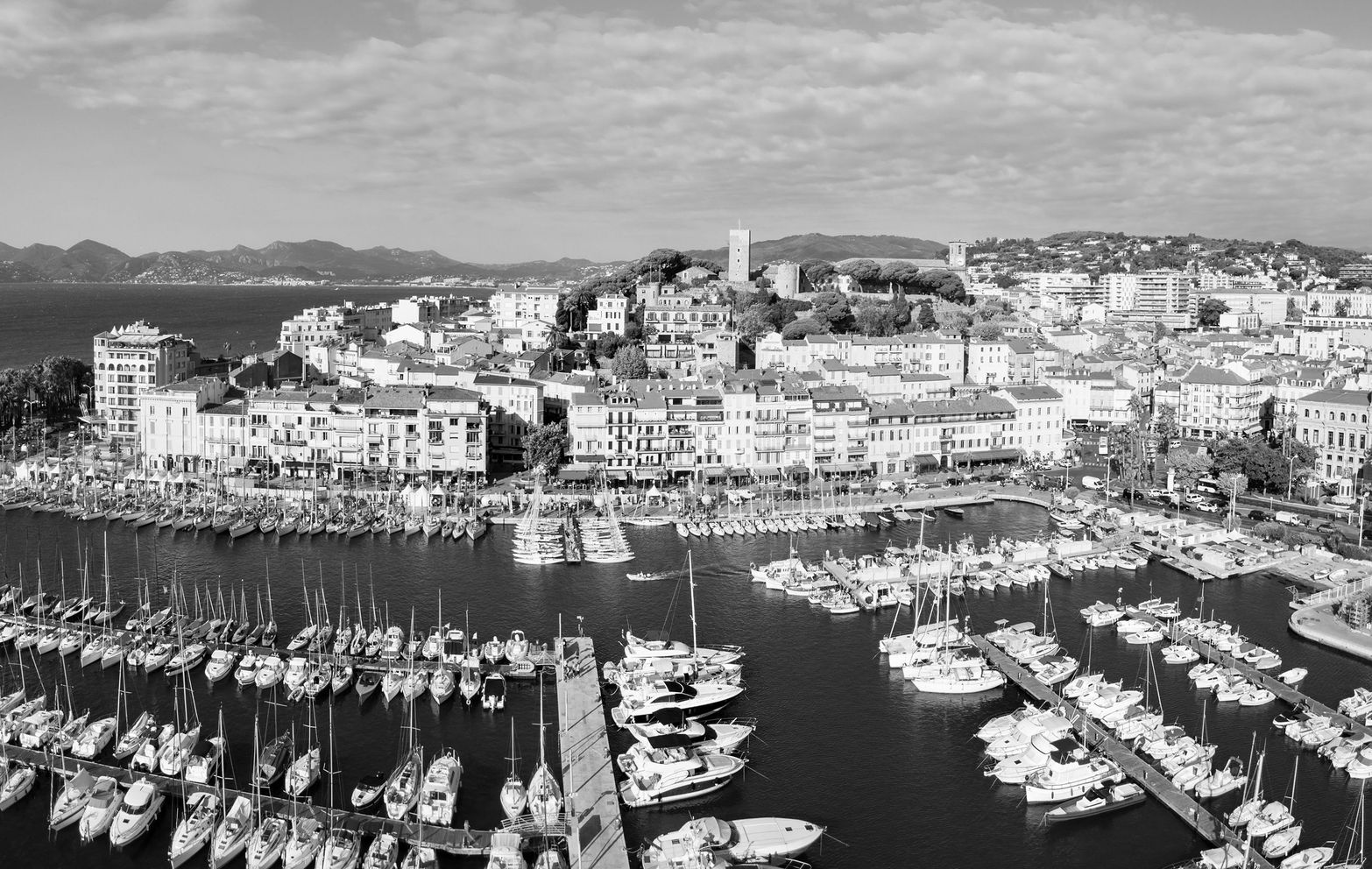 Black and white aerial captures a large marina teeming with boats and a coastal city.