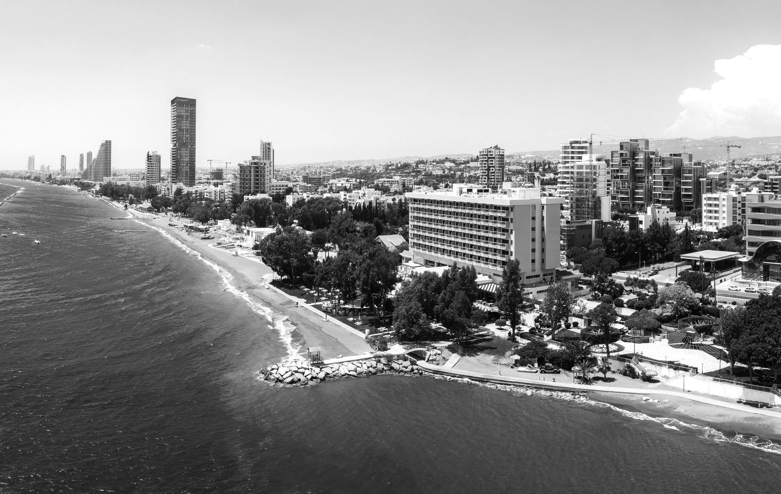 Black and white aerial view of a city coastline with tall buildings and ocean waves.